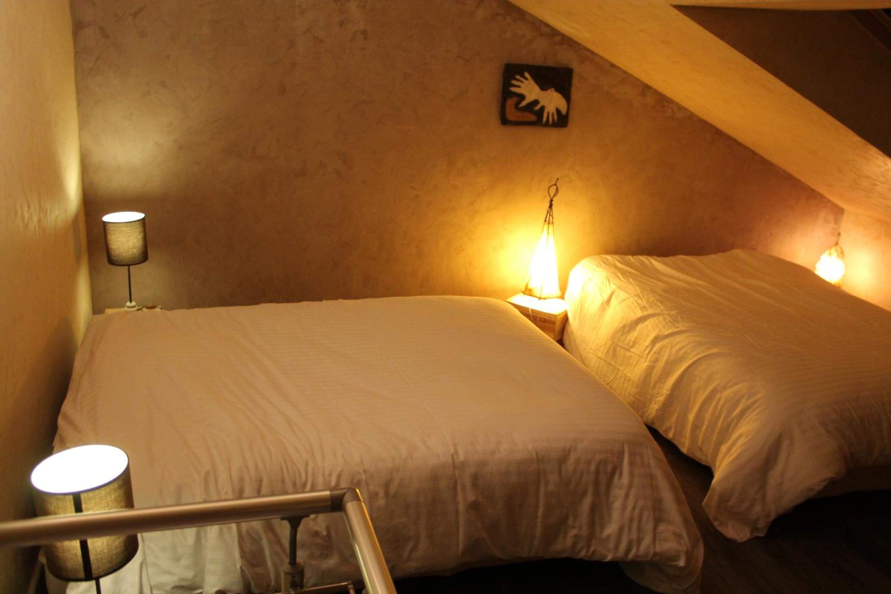 Una habitación pequeña y con poca luz, con dos camas, una lámpara y una obra de arte en la pared.
