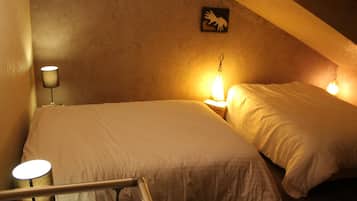 Una habitación pequeña y con poca luz, con dos camas, una lámpara y una obra de arte en la pared.