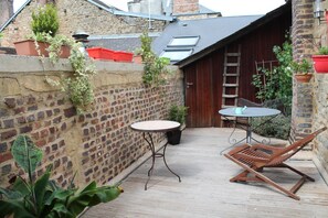 A patio with a table and a chair, a brick wall, and potted plants. - Côté Chambres (Charleville-Mezieres)