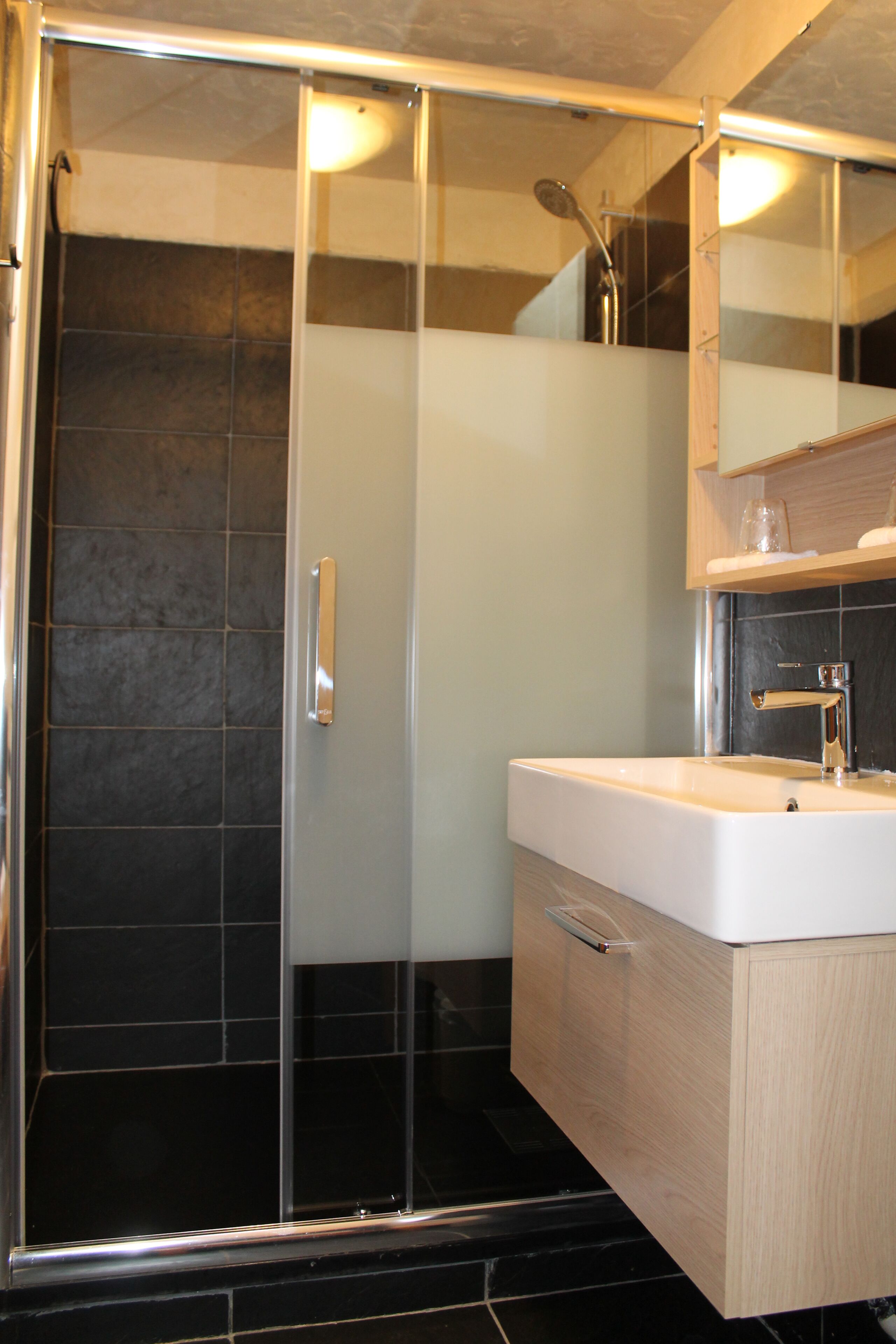 Un baño moderno con ducha envuelta en vidrio, un lavamanos blanco y un mueble de tocador de madera.