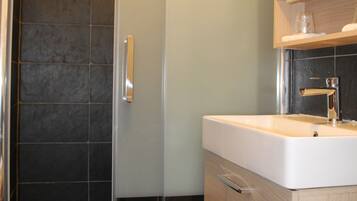 Un baño moderno con ducha envuelta en vidrio, un lavamanos blanco y un mueble de tocador de madera.