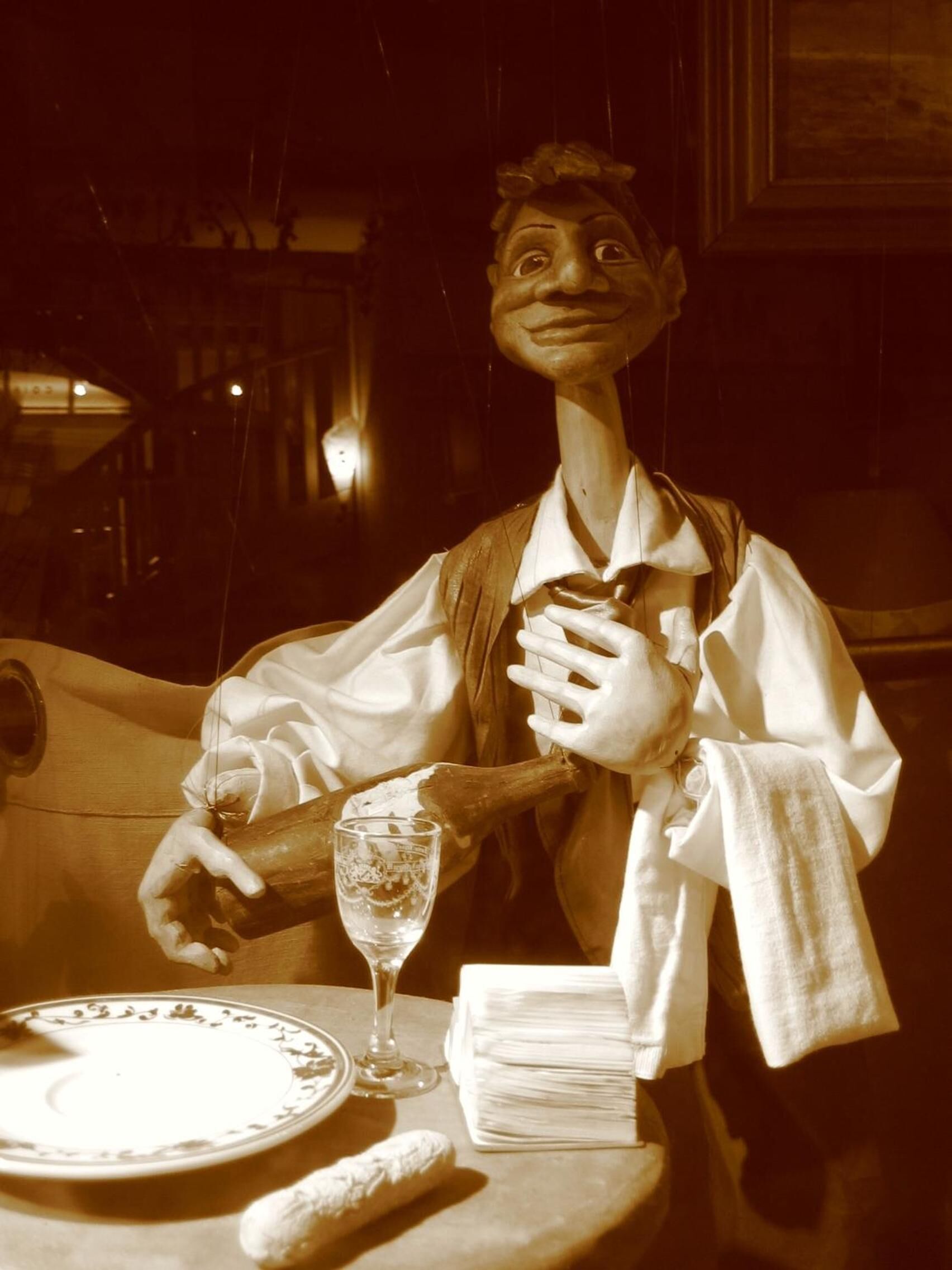 A puppet with a plate, a glass, and a napkin on a table.