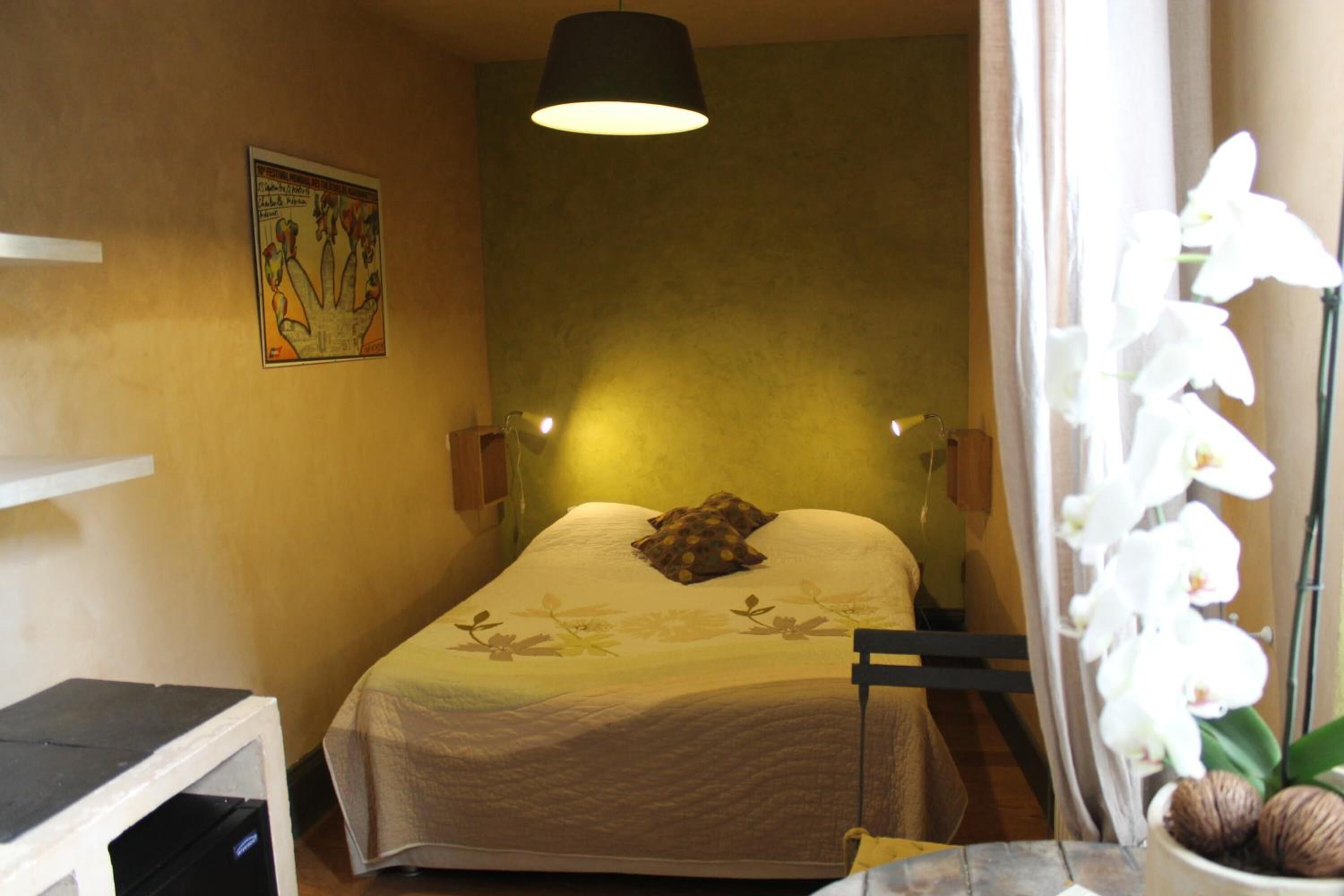 Un dormitorio con una cama, lámparas de noche, un escritorio, un espejo y una orquídea en maceta.