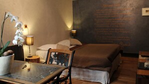 A bedroom with a bed, a table with a potted orchid, a chair, and a wall with text. - Côté Chambres (Charleville-Mezieres)