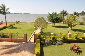 A well-maintained garden with a paved pathway leading to a gate, surrounded by manicured lawns and palm trees, overlooking a body of water.