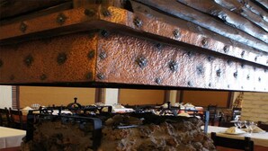 Un interior rústico con paredes de ladrillo visto y techo de metal. Las mesas están preparadas con manteles blancos y copas de vino.