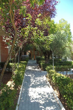 A paved pathway flanked by greenery and a brick building. - La Fuensanta (Horche)