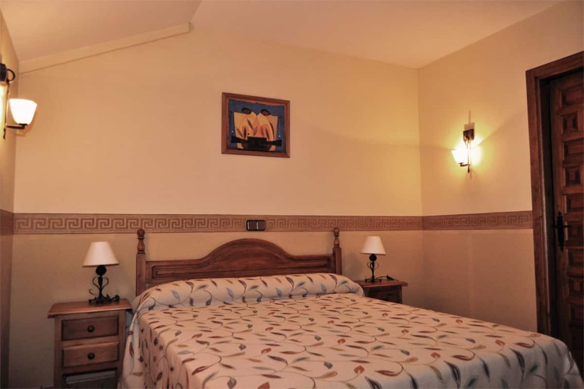 Une chambre d’hôtel comprenant un lit, deux tables de chevet avec des lampes, une œuvre d’art accrochée au mur et une porte.