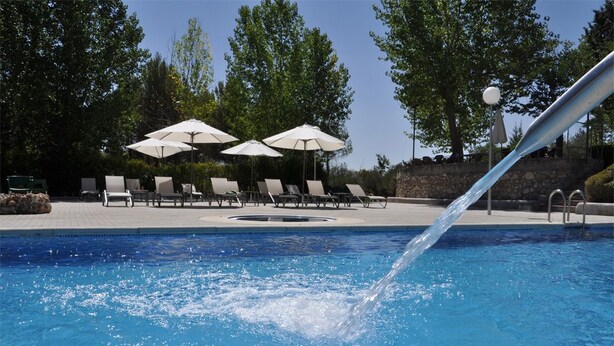 Una piscina con agua cayendo, rodeada de sillones de descanso y sombrillas.