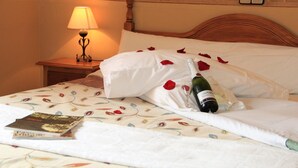 Una cama bien hecha, con una botella de vino, copas y pétalos de rosa.
