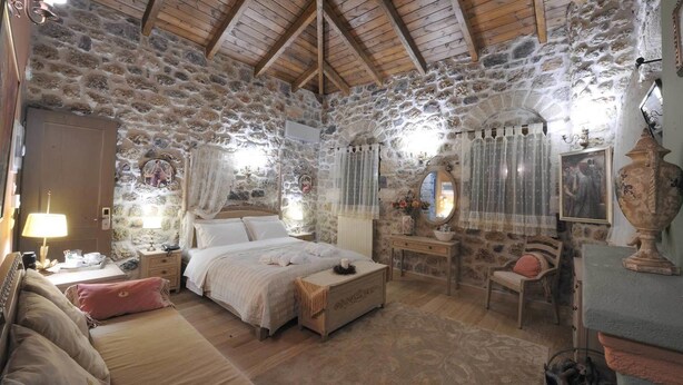 Une chambre rustique aux murs de pierre, avec un plafond en bois, un lit, un bureau et une chaise.