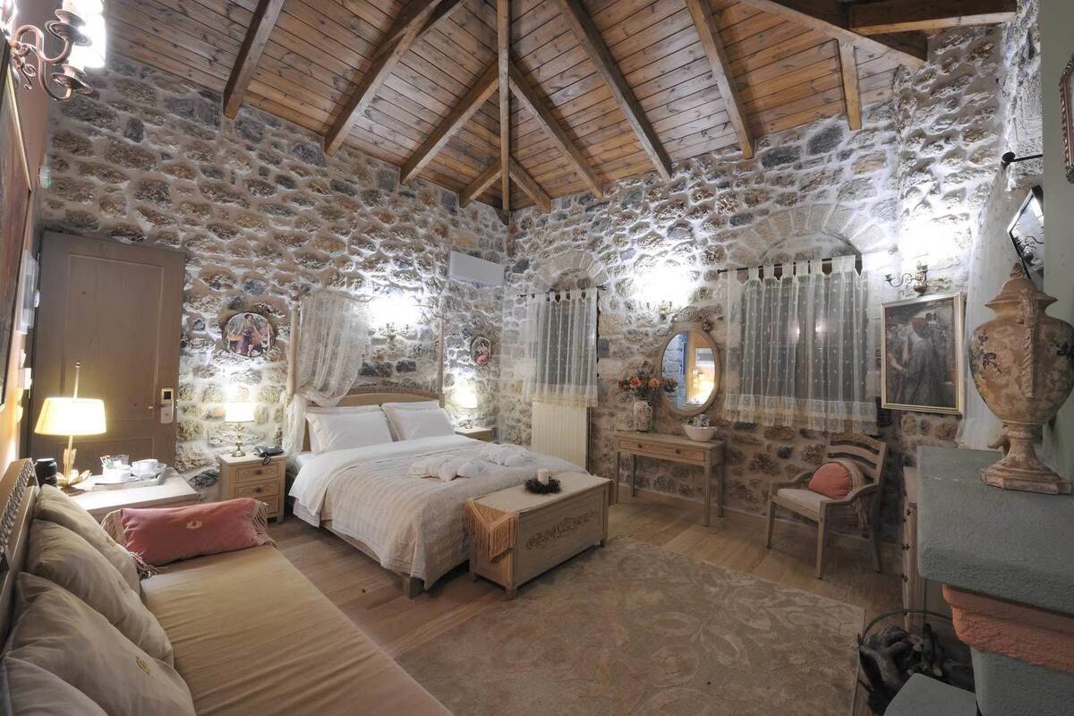 Une chambre rustique aux murs de pierre, avec un plafond en bois, un lit, un bureau et une chaise.
