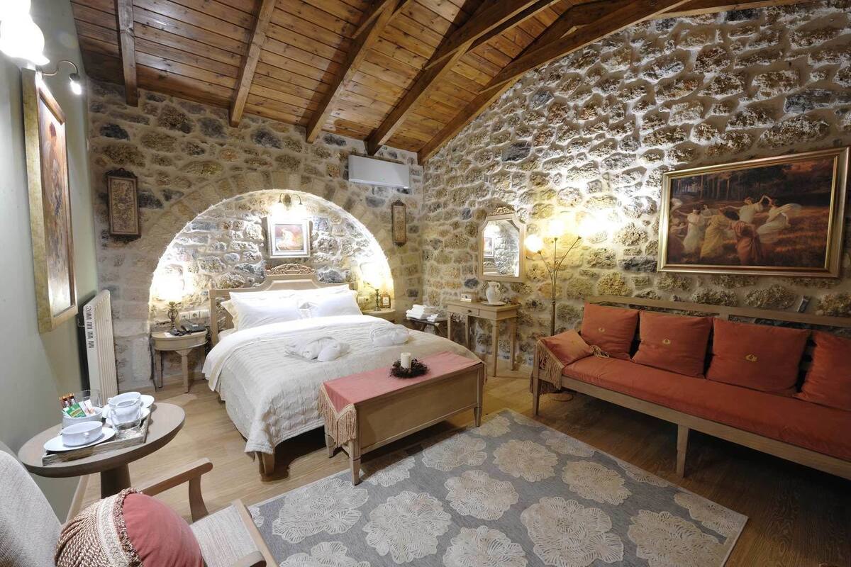 Une pièce rustique avec un mur en pierre, un lit recouvert de draps blancs, un canapé rouge et un tableau accroché au mur.