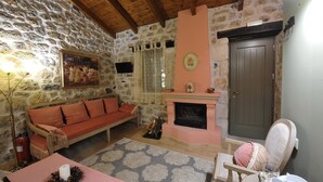 Un salon chaleureux avec un mur en pierre, un canapé rose, une cheminée et un plafond en bois.