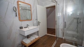 Un baño moderno con tocador de mármol, cabina de ducha de vidrio y estante de madera con toallas.