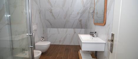 A bathroom with a glass shower enclosure, a toilet, a sink, and a mirror.