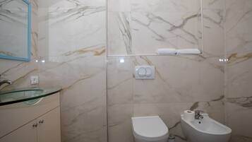 Une salle de bain avec un lavabo en verre, des toilettes et un bidet.