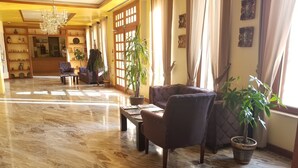 Un hall espacioso con piso de mármol, una araña y una zona de estar con sofá y sillones, además de plantas en macetas.