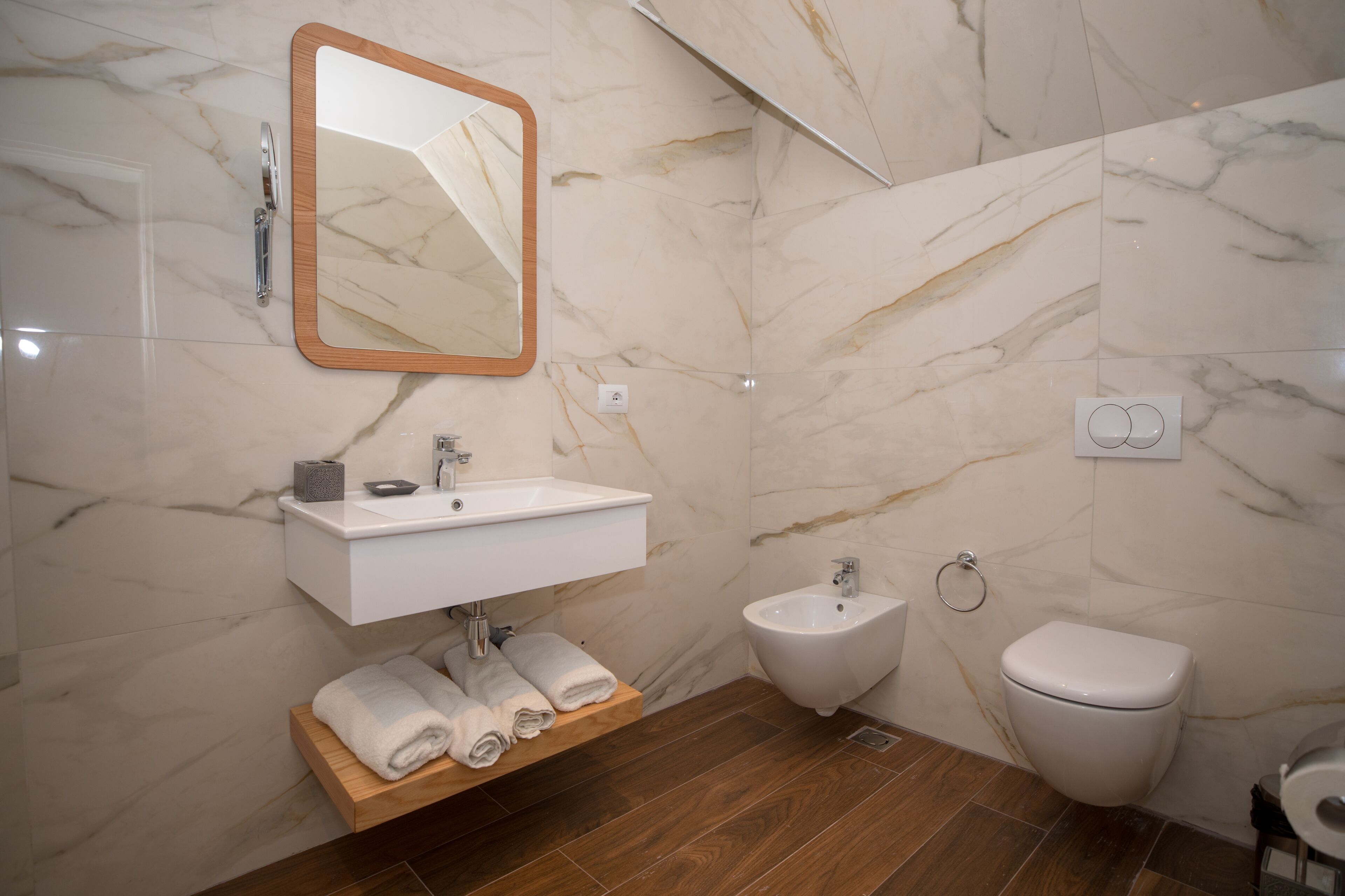 Ein modernes Badezimmer mit Marmorwand, Waschtisch aus Holz, einem Waschbecken, einem Bidet und einer Toilette.