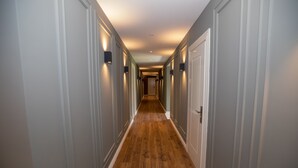 Un pasillo largo y estrecho con suelo de madera y paredes blancas, que conduce a una puerta al final.