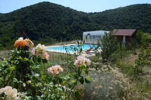 A pool area with a house in the background, surrounded by greenery and hills. - Chambres Et Tables D'Hote De Margaridou (Blesle)
