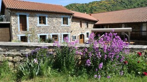 A stone building with a red-tiled roof, multiple windows, and a stone wall in front. - Chambres Et Tables D'Hote De Margaridou (Blesle)