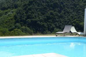 Una piscina con dos tumbonas y vistas a una ladera boscosa.