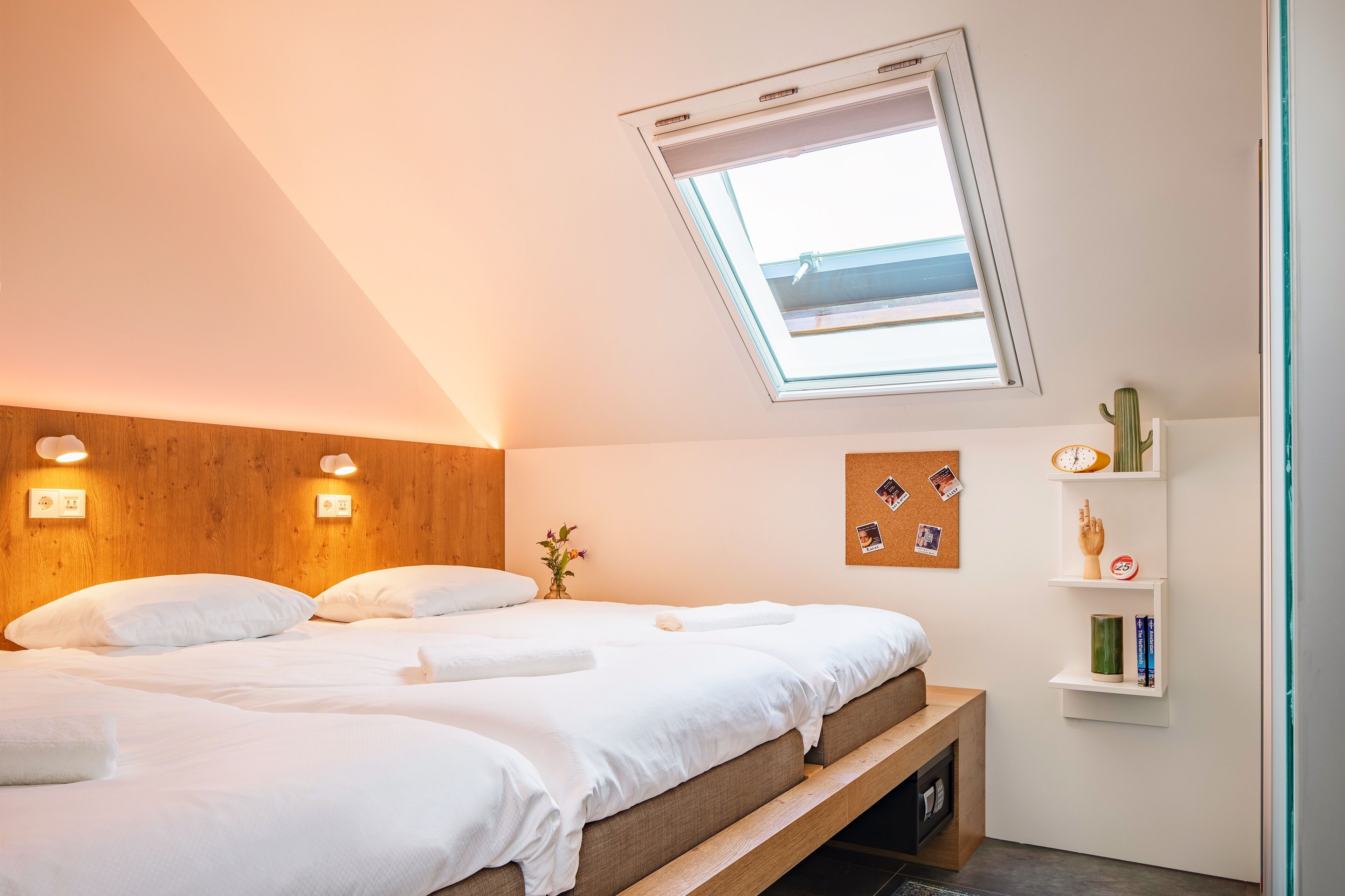 Une chambre avec deux lits, une lucarne, des étagères murales et un banc en bois.