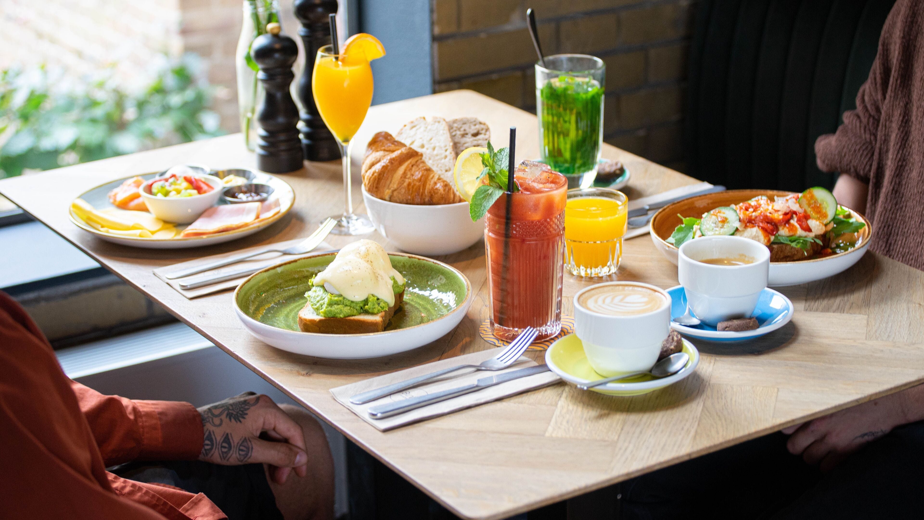 A table set with breakfast items including toast, eggs, a green smoothie, and a Bloody Mary.