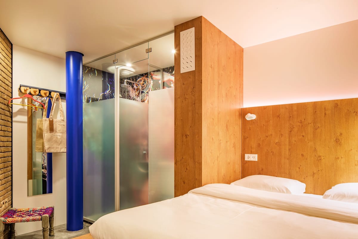 A hotel room with a bed, a bench, a wardrobe, and a sliding door.