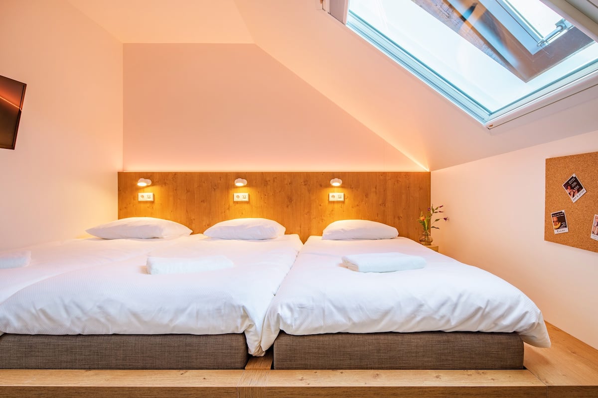 A twin room with two beds, wooden headboard, skylight, and a corkboard with photos.