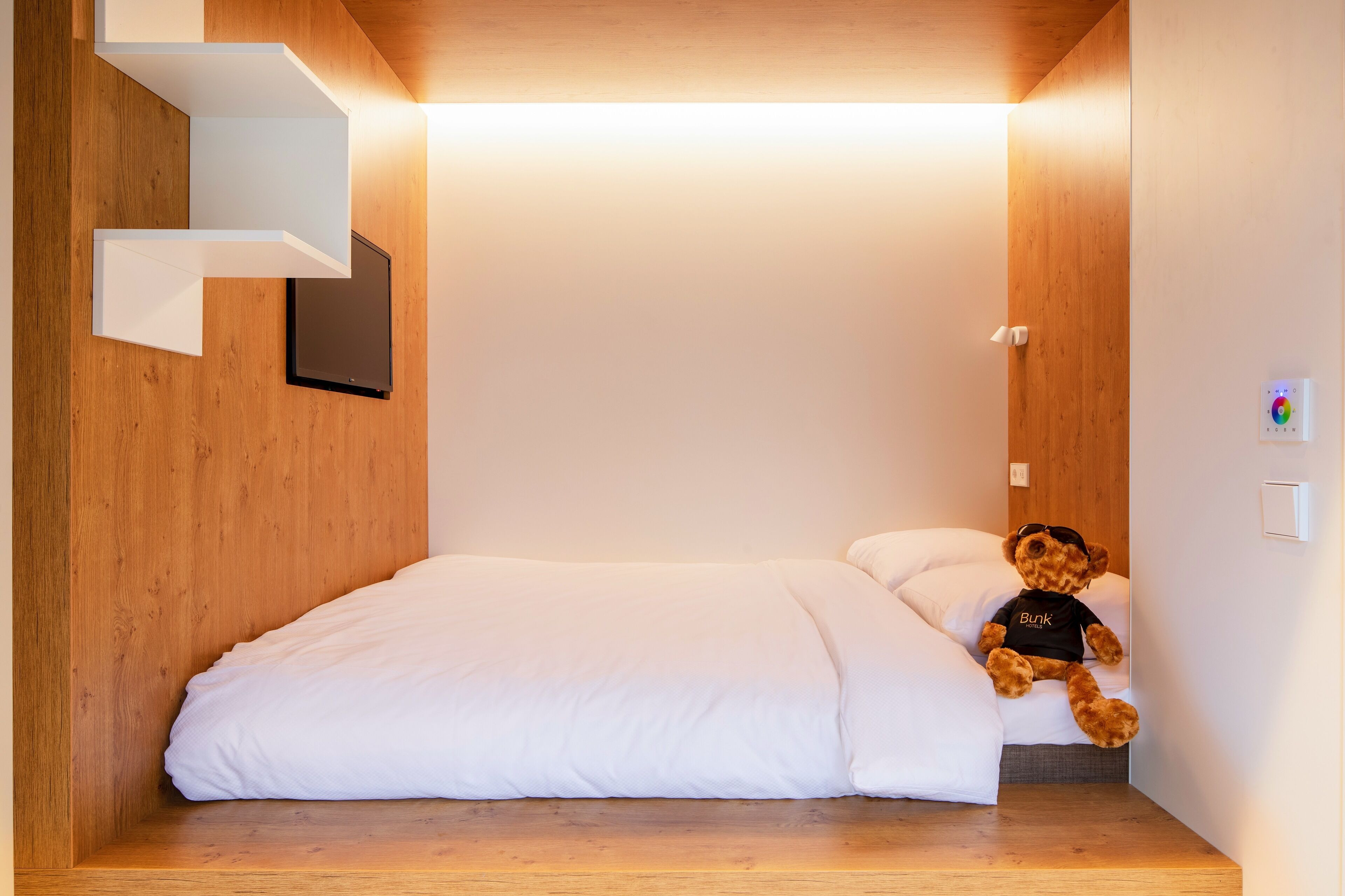 Un dormitorio moderno con cabecera de madera, cama blanca y un osito de peluche sobre la cama.