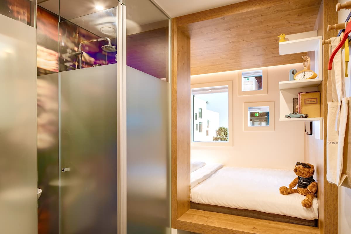 A compact bedroom with a bed, a teddy bear, and a window.