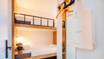 Habitació amb lliteres, un os de peluix al llit inferior, una tovallola blanca i una bossa amb la inscripció 'HOLY MESS' a la paret.