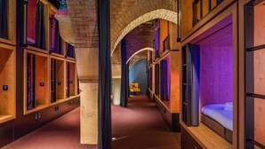 A hotel corridor with wooden bunk beds, a brick archway, and a purple-lit room in the distance. - Bunk Hotel Amsterdam (Amsterdam)