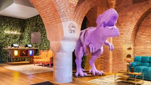 A room with a large dinosaur statue, a check-in counter, a sofa, and a coffee table. - Bunk Hotel Amsterdam (Amsterdam)
