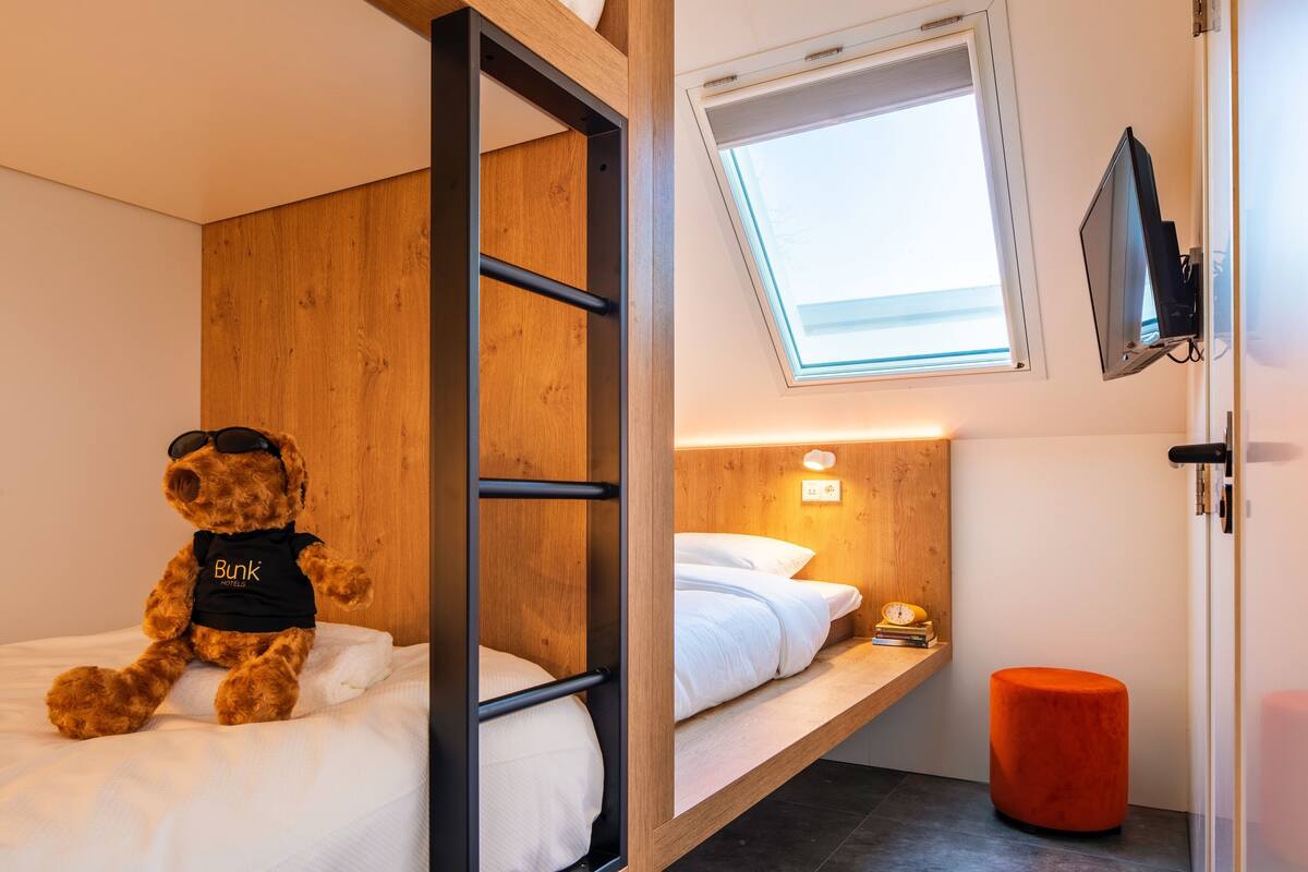A bunk bed with a teddy bear on the lower bunk, a skylight above, and a television mounted on the wall.
