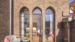 A brick building with three arched windows, a wooden deck, a chair, a small table with a vase, and a flamingo decoration. - Bunk Hotel Amsterdam (Amsterdam)