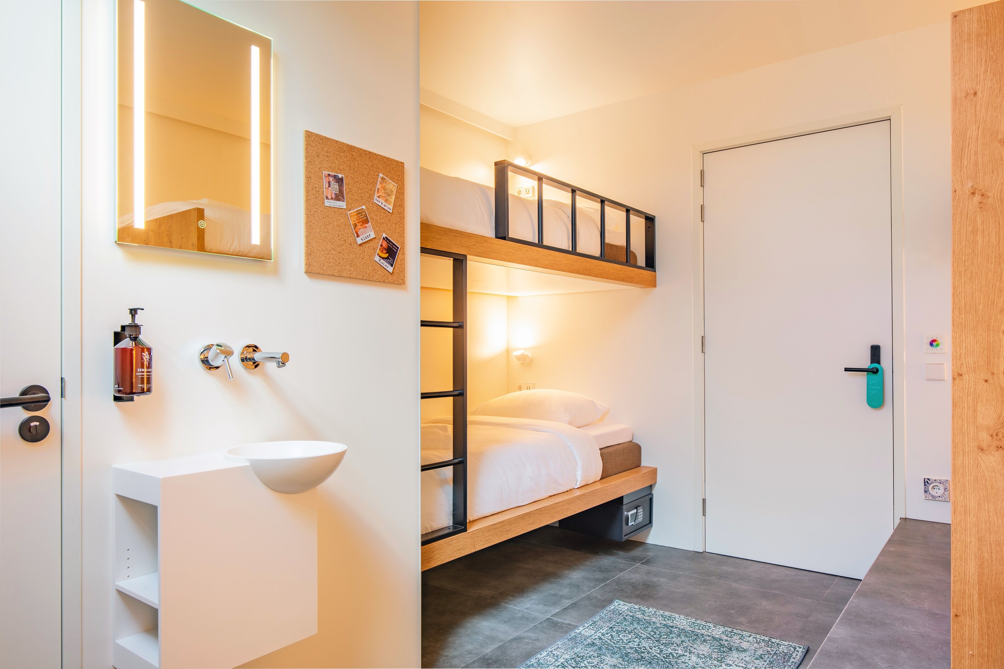 A modern bathroom with a white sink, a mirror, and a corkboard on the wall.