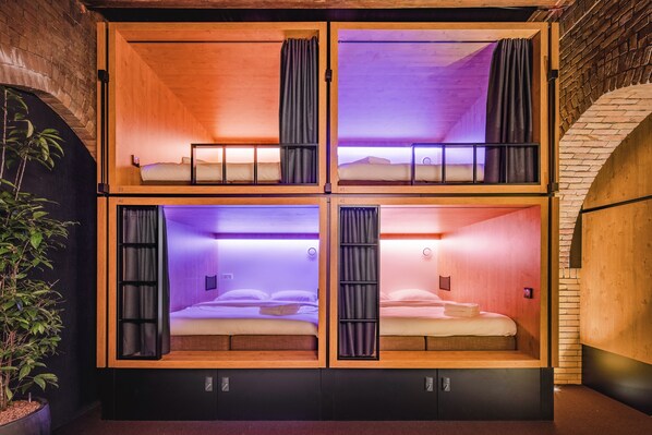 A four-room cabin with wooden walls and a brick archway. Each room has a bed and a small window. - Bunk Hotel Amsterdam (Amsterdam)