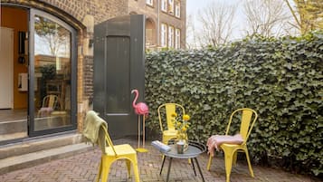 Un patio con sillas amarillas, una mesa con un jarrón y un libro, y una puerta negra.
