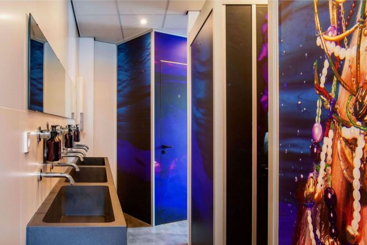 Un baño moderno con un espejo grande, dos lavamanos y una puerta con un diseño abstracto en azul y morado.