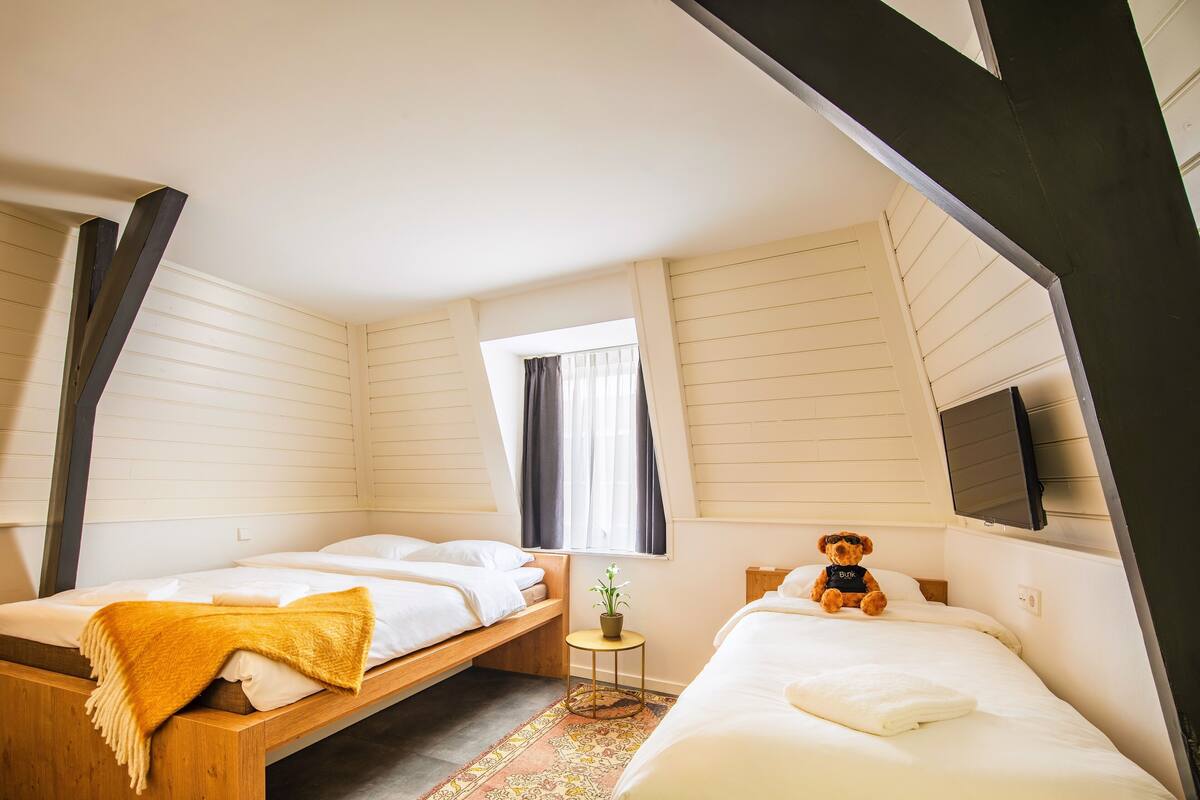A bedroom with two beds, a small table with a plant, and a teddy bear.