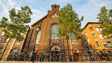 Un edificio histórico con un arco pronunciado y una torre del reloj, rodeado de árboles y bicicletas.