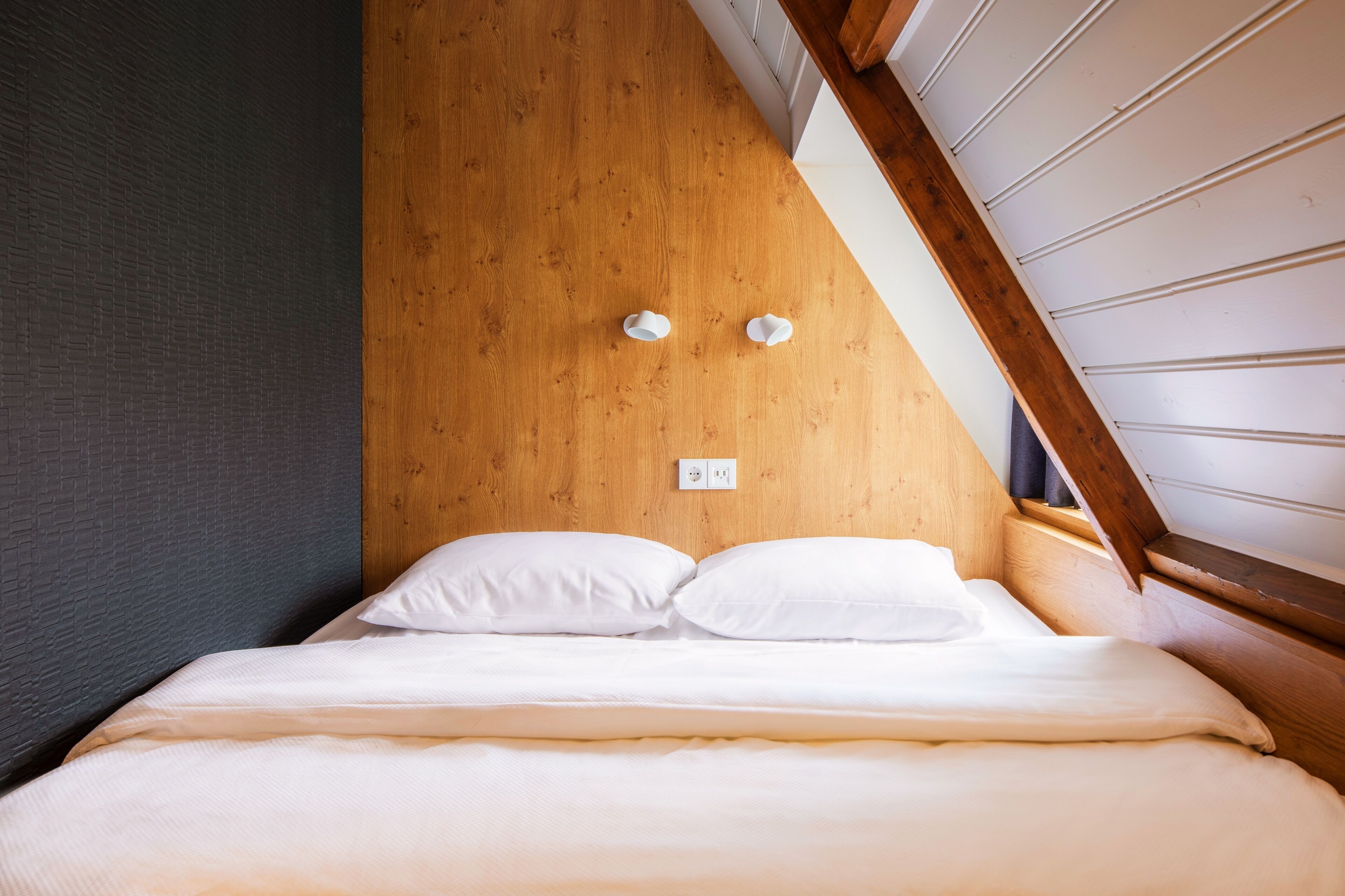 A bed with white bedding, a wooden headboard, and a slanted ceiling.