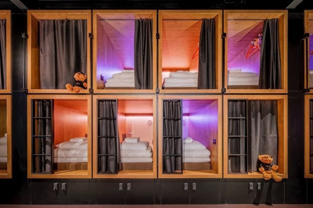 Habitación de hotel con varias camas, cada una con estructura de madera y cortinas negras.