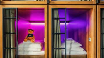A hotel room with a wooden bunk bed, a teddy bear on the lower bunk, and purple lighting.
