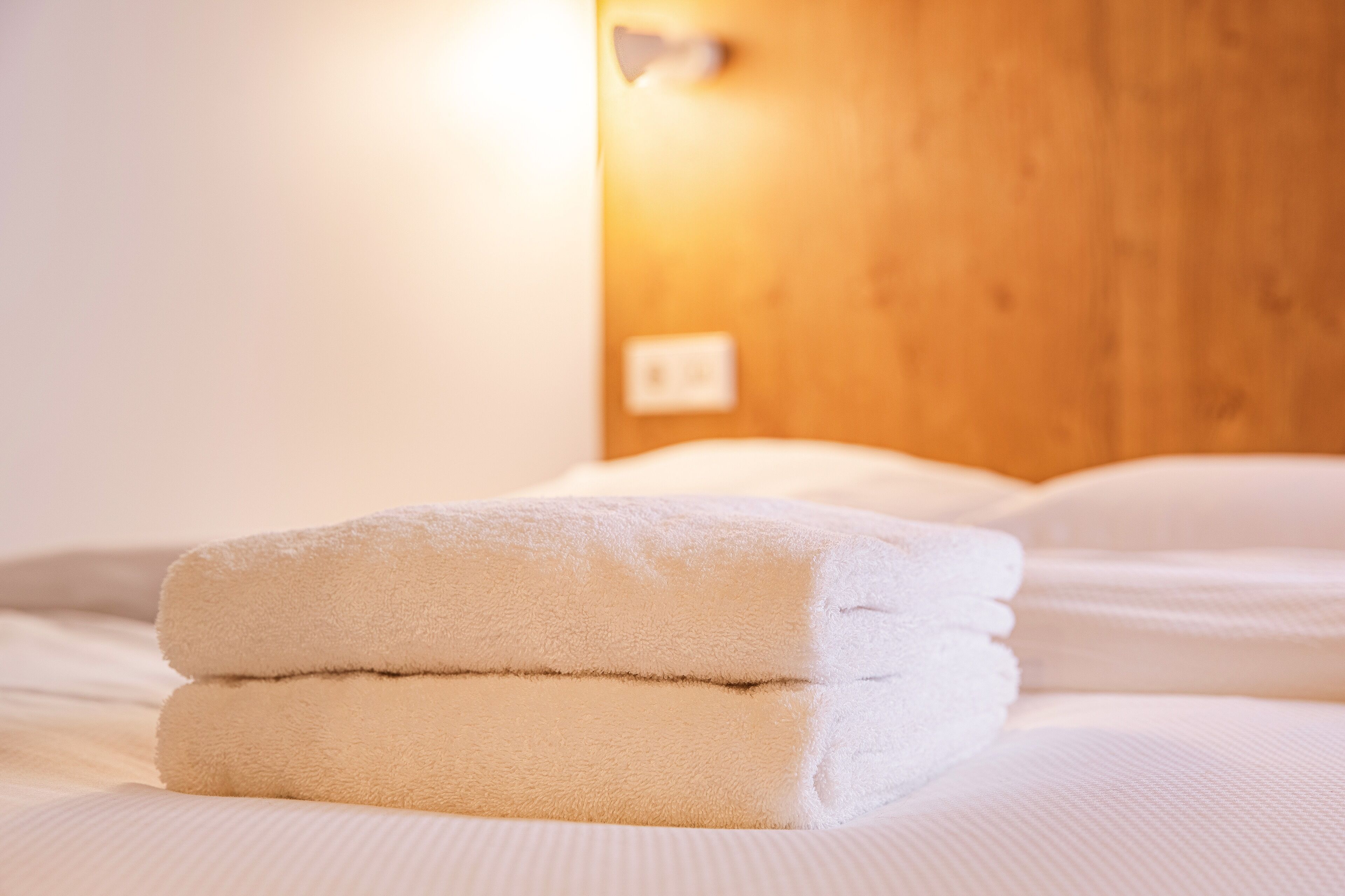 Un letto rifatto con asciugamani bianchi piegati e una testiera in legno.