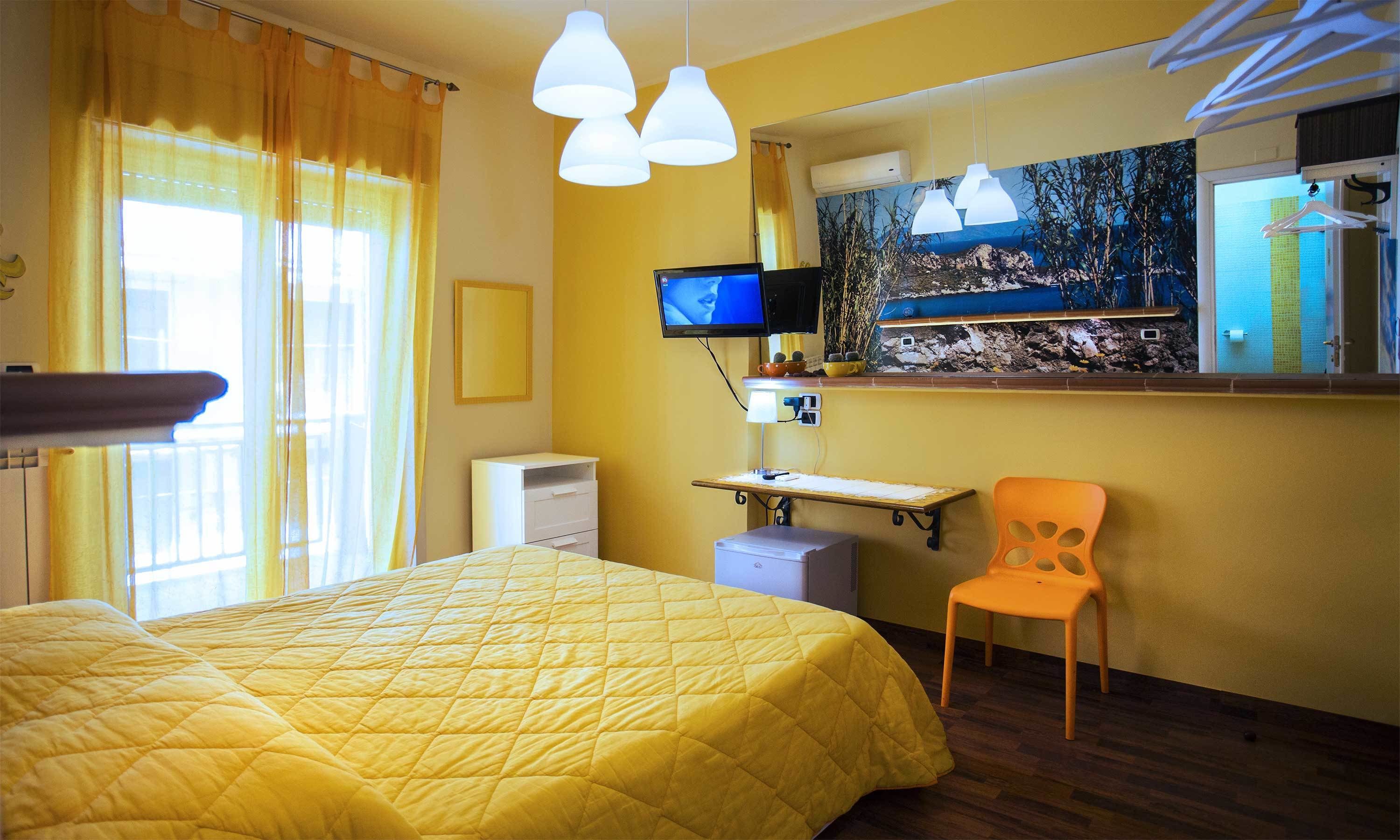 A hotel room with a bed, a desk, a chair, a television, and a window with curtains.