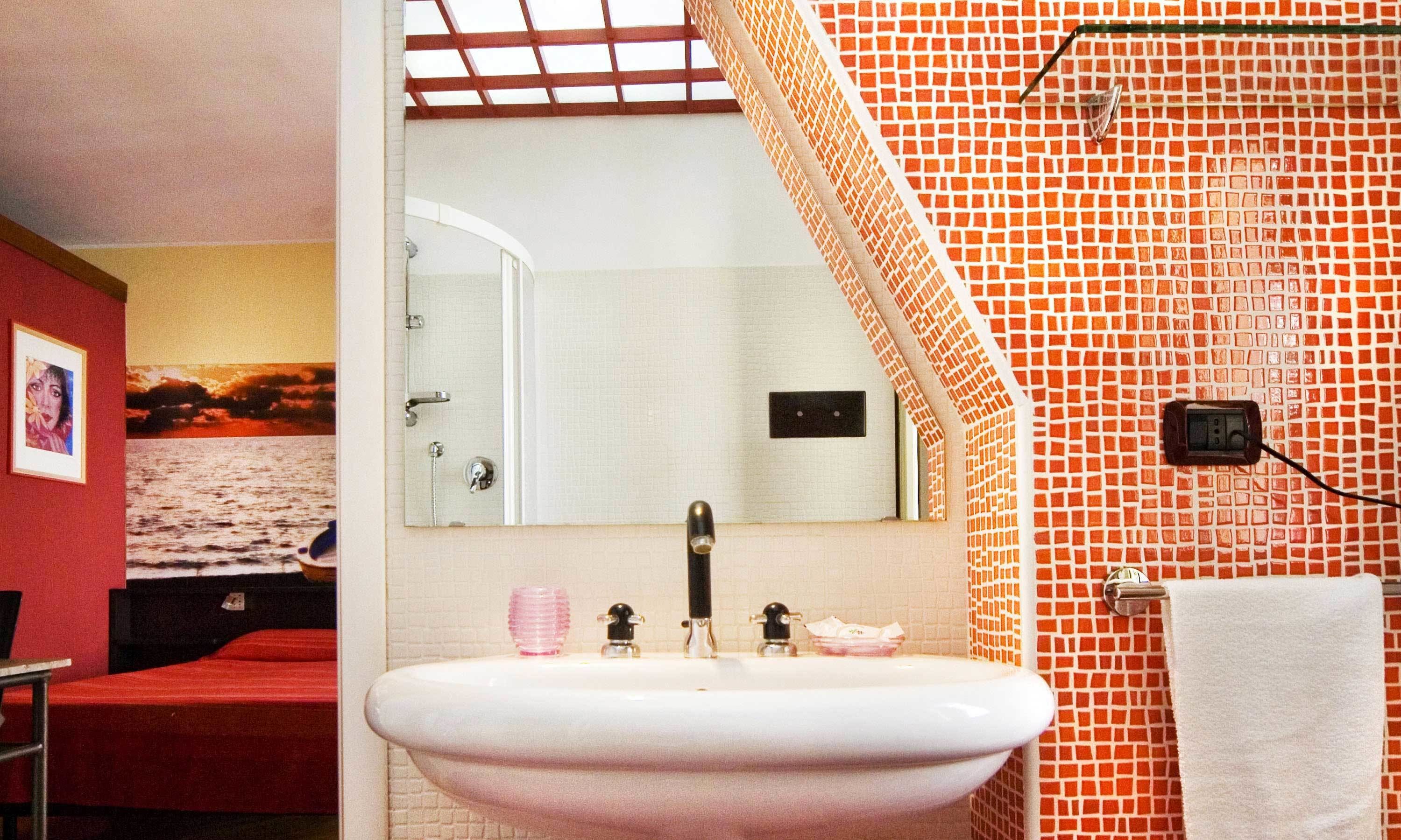 Un baño con un lavamanos blanco, un espejo y una pared con estampado rojo y naranja.